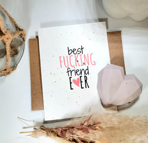 White seed paper greeting card says "Best fucking friend ever" with pink concrete heart and feathers for decor