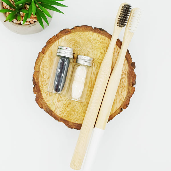 Plain and white bamboo toothbrushes with corn and bamboo compostable dental floss containers.