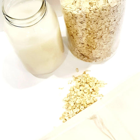 Nut milk bag with oats spilling out and oats in glass container next to oat milk in mason jar.