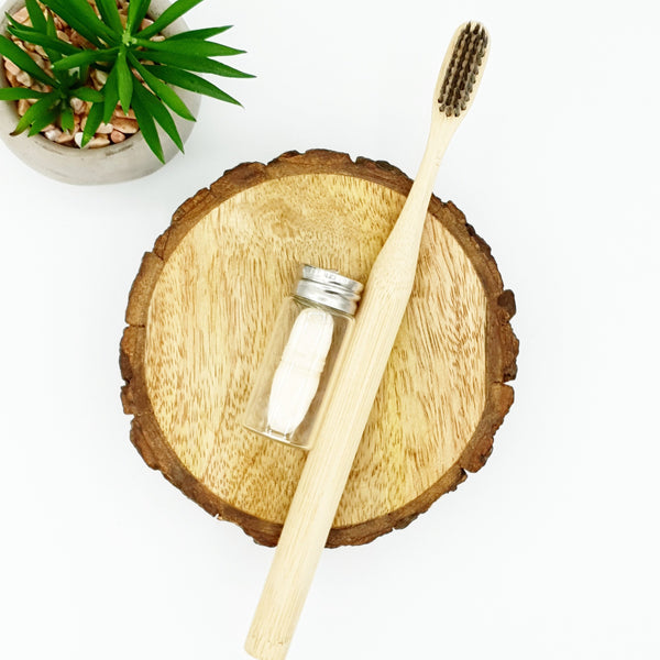 Plain bamboo toothbrush next to compostable corn dental floss in glass container.
