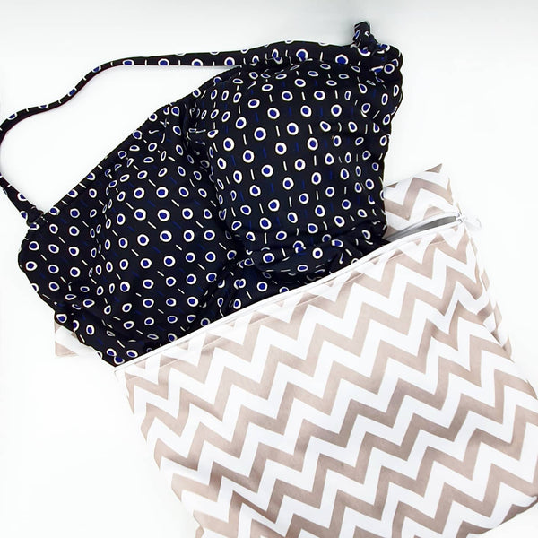 Large reusable waterproof bag with swimsuit coming out of it.  Grey chevron pattern.