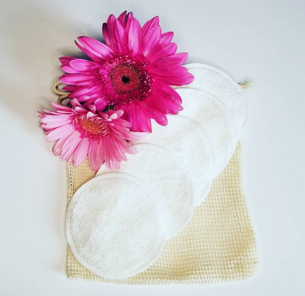 5 pack cotton terry reusable makeup remover pads with mesh laundering bag and two pink gerbera daisies.